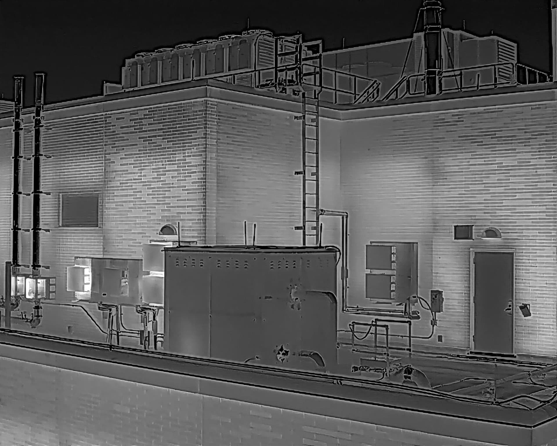 Thermal image of a rooftop with mechanical equipment, ductwork, a ladder and railings, and the brick wall of a taller section behind